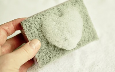 Image of a persons hand holding a cleaning sponge, with soap bubbles in a heart shape on