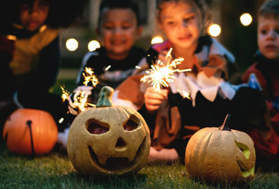 Image of children sat in a garden with pumpkin lanterns on Halloween