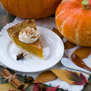 Image of a slice of pumpkin pie on a plate next to a pumpkin