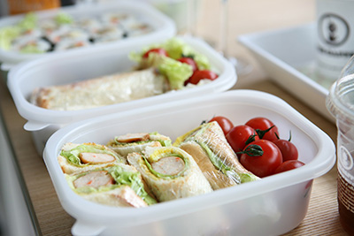 Image of a lunchbox with food in and a sandwich wrapped in Cling Film