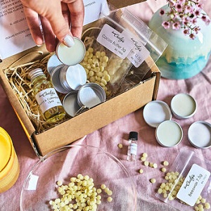Image of a Make Your Own Lip Balm Kit, including shea butter, beeswax, cocoa butter, almond and calendula oil, a fragrance, five empty pots, five blank white labels, and instructions.