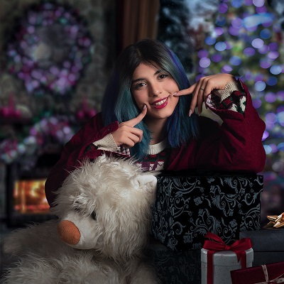 image of a teenage girl smiling next to a large teddy bear in front of a Christmas tree